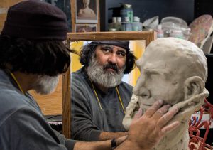 Man looking in mirror while making a bust out of clay