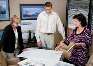 Two women and a man in executive office look at blueprints